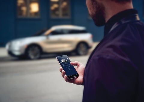A person is shown interacting with a smartphone to connect to a Lincoln vehicle across the street. | Stivers Lincoln (AL) in Montgomery AL