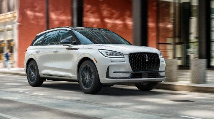 A white 2025 Lincoln Corsair® SUV with the Jet Appearance Package is being driven through a city.| Stivers Lincoln (AL) in Montgomery AL