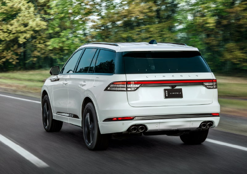 A white 2026 Lincoln Aviator® SUV is being driven away down a road lined with colorful trees. | Stivers Lincoln (AL) in Montgomery AL