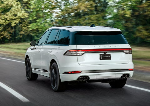 A white 2026 Lincoln Aviator® SUV is being driven away down a road lined with colorful trees. | Stivers Lincoln (AL) in Montgomery AL